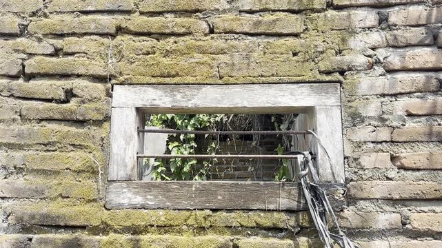 Old weathered brick wall with small ventilation window and metal bars