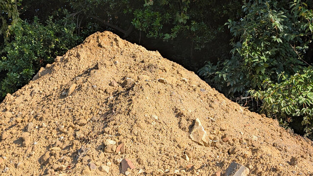 Pile of excavated dirt and stones in front of green trees