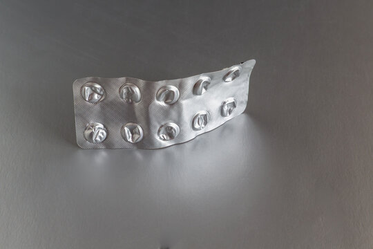 Empty silver blister pack from pills lying on a grey surface.