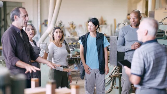 Group of woodworkers listening to their supervisors during a morning briefing in a carpentry workshop. Skilled artisans discussing a project