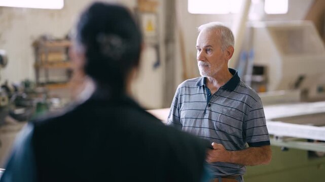 Elderly manager holding a tablet and talking with his female apprentice. Two colleagues discussing a new project in a carpentry workshop