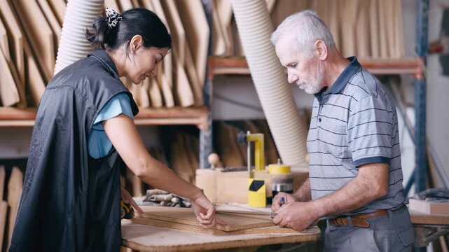 Senior craftsman mentoring a female apprentice in a carpentry workshop. Two woodworkers collaborating on a project and talking about wood planks