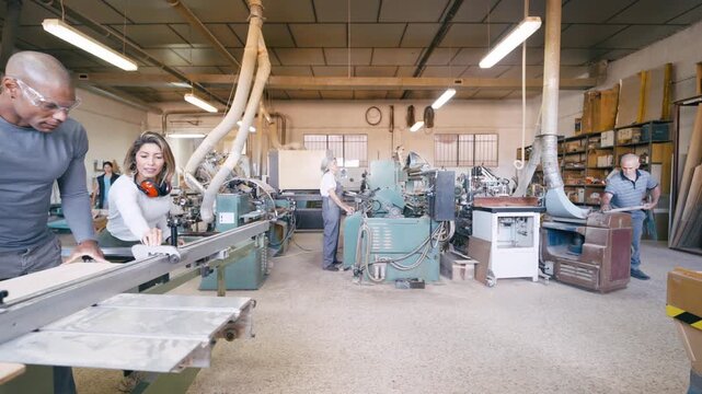 Busy carpentry workshop with skilled artisans working. A man and a woman use a table saw while colleagues operate other industrial machines