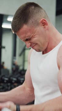 Man performing weightlifting exercise in well lit gym setting. Close up view shows focused effort as man uses fitness equipment with visible weights and workout environment