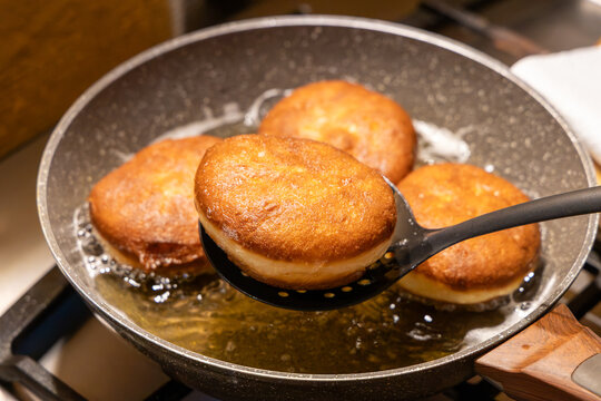 Taking out fresh golden doughnut from hot frying oil with skimmer spoon for traditional Fat Thursday dessert preparation and delicious homemade sweet pastry cooking.