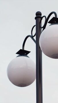 Two white round globe shaped lamps mounted on black metal pole. background is consistently gray and featureless suggesting cloudy weather or overcast day