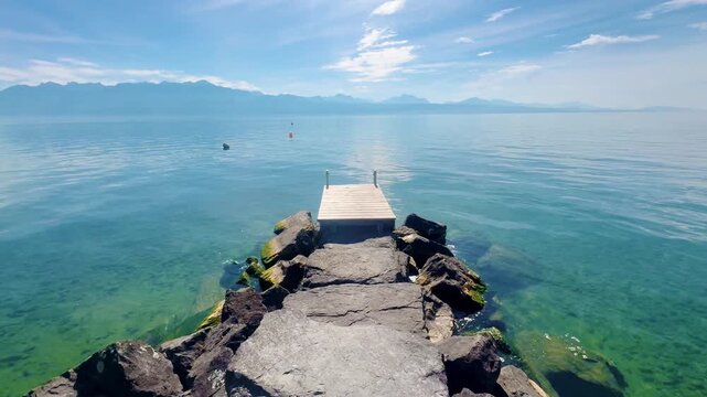 POV Walking Along Rocky Pier Over Clear Lake Water to Horizon in Switzerland
