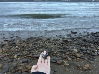 Woman's hand holding a single, naturally opened blue mussel shell forming a perfect heart shape, against a pebbly beach and ocean waves in overcast weather. © Карiна Дiденко