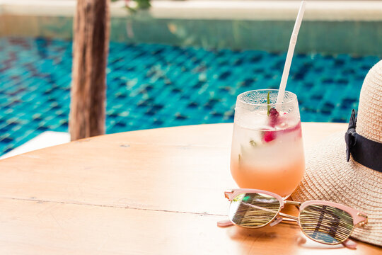 Lychee soda cocktails sunglasses and straw hat on table with blurred poolside background. Summer drinks concept.