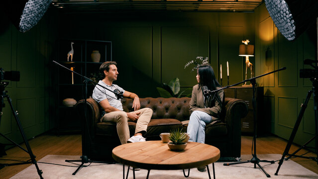 Man and woman producing a digital podcast, discussing topics into microphones during a video recording session in a professional studio