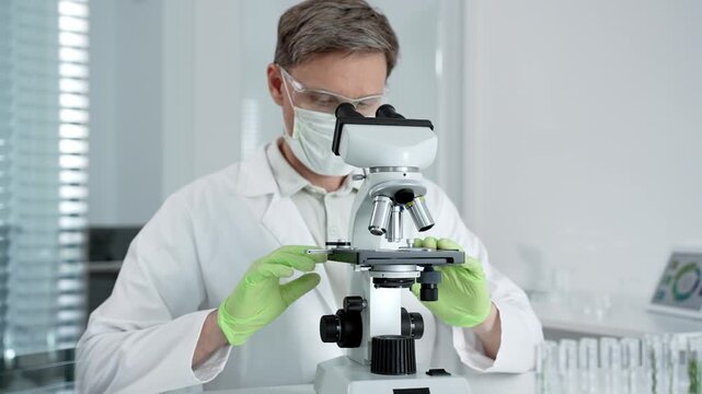 Research scientist looking through a microscope. Adjusting the focus and objective to analyze a specimen