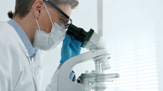 Scientists focus at a microscope in a bright laboratory, performing medical research and contributing to advancements in science, health, and biomedical technology