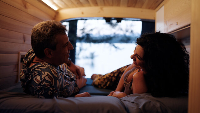Mature couple relaxing and talking inside a cozy camper van, enjoying the warmth and comfort during a road trip