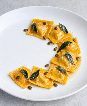 Fresh pumpkin ravioli garnished with crispy sage leaves and toasted pumpkin seeds on a white plate