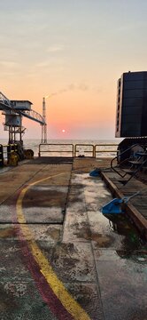 Eye level landscape photo of a workboat deck facing the ocean during a warm sunset with an offshore flare in the background, great for energy sector marketing and maritime logistics materials.