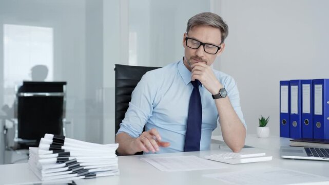 Businessman's hands analyzing financial data on paper documents and a laptop spreadsheet, using a calculator to manage accounting and budget planning in an office setting