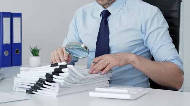Mature businessman investigating financial documents with a magnifying glass. Performing detailed analysis. Scrutinizing reports