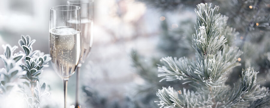 Two glasses of champagne with frozen branches in a snowy winter landscape. Horizontal background with fetsive bokeh for christmas and new year greetings.