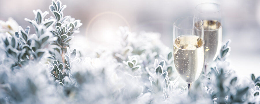 Two glasses of champagne with frozen branches in a snowy winter landscape. Horizontal background with fetsive bokeh for christmas and new year greetings.