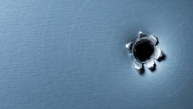 Single bullet hole in a blue metal surface with visible impact damage and circular stress marks