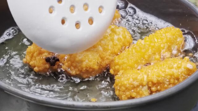 Flipping crispy golden nuggets deep frying in hot bubbling oil with skimmer spoon in camping pan
