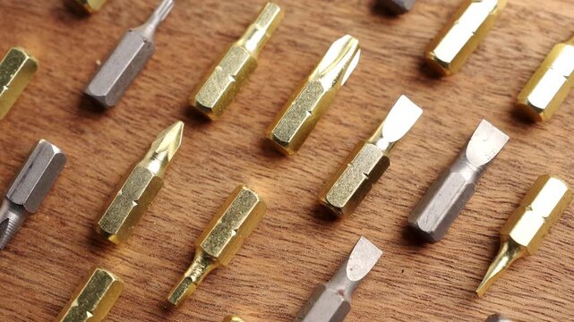 Assorted metal screwdriver bits neatly arranged on a wooden workbench. Rotation