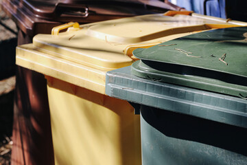 Colorful outdoor waste containers. Yellow green brown garbage bins. Household recycling equipment background. Municipal waste sorting concept. Plastic wheelie bin lids. Refuse collection system.