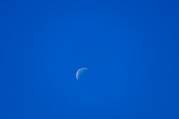 Minimalist shot of a crescent moon visible in the clear blue sky during daytime, daytime astronomy. © Kiril