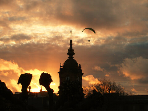 Nubes doradas al atardecer con las siluetas de una iglesia, arboles y un parapente volando
