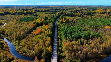 Fototapeta premium Aerial view of railway bridge surrounded by vibrant autumn foliage and winding river