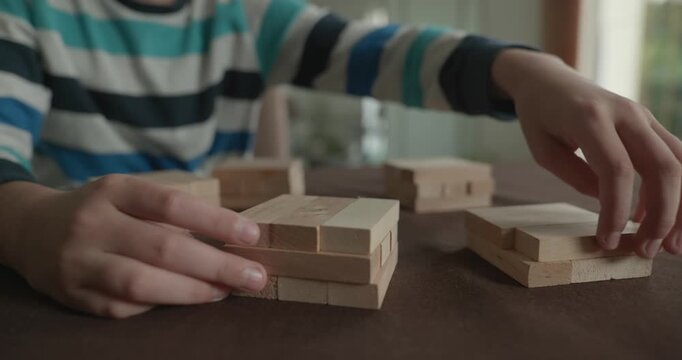 Close-up children's hands play with wooden bricks constructing structures. 4K 10-bit