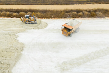 An aerial view of heavy machinery including a dump truck unloading soil, a bulldozer, and a grader working on a road construction embankment. © scharfsinn86