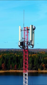 5G 6G Telecommunication tower with technician performing maintenance on the upper section amidst fall foliage