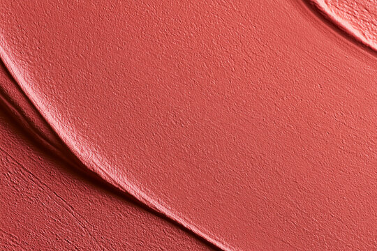 Coral red cosmetic smear with textured strokes, showing beauty product swatch and creamy makeup background