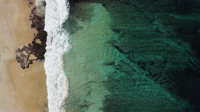 An ocean wave breaks along a turquoise coloured, pristine, reef-lined sandy shore. Filmed on a beautiful idyllic sunny day from high above the beach on the South Coast of New South Wales, Australia.