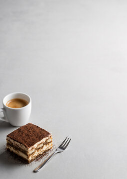 Classic Italian tiramisu cake slice with espresso coffee cup and dessert fork on grey concrete background copy space vertical