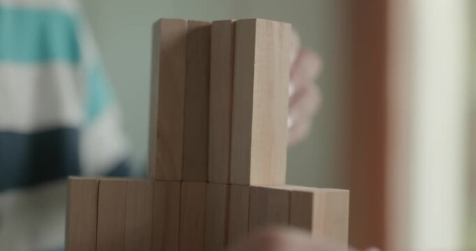Close-up children's hands play with wooden bricks constructing structures. 4K 10-bit