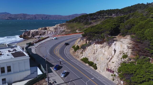 Aerial view tracks curved Point Lobos Avenue leading past coastal cliffs toward Sutro Baths ruins and the Pacific Ocean coastline in San Francisco, California.
