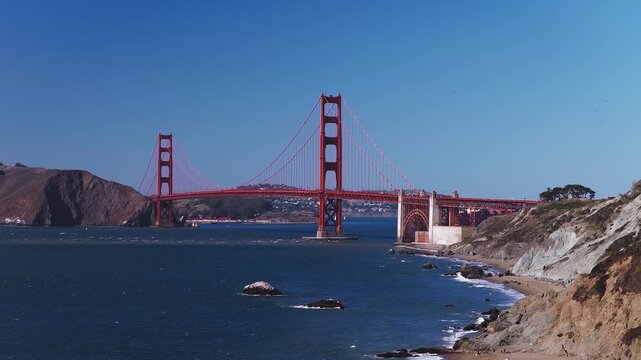 The Golden Gate Bridge spans across the entrance to San Francisco Bay with Marshall's Beach and coastal bluffs below under a clear sky in California.