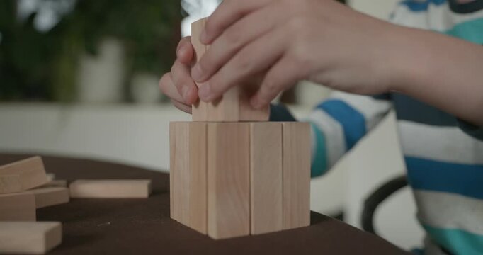 Close-up children's hands play with wooden bricks constructing structures. 4K 10-bit