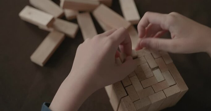 Close-up children's hands play with wooden bricks constructing structures. 4K 10-bit