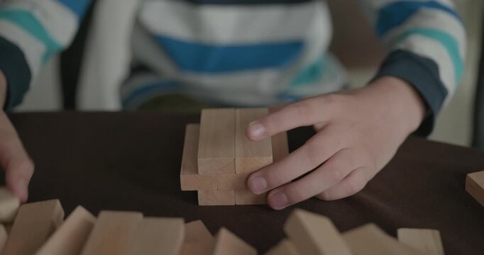 Close-up children's hands play with wooden bricks constructing structures. 4K 10-bit
