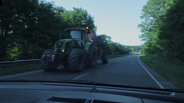 Windshield View of a Car Passing an Oncoming Tractor on a Tree-Lined Road