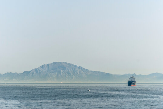 Cargo ship sailing near the Rock of Gibraltar with Jebel Musa of Rif Mountains in Morocco, Africa in the background