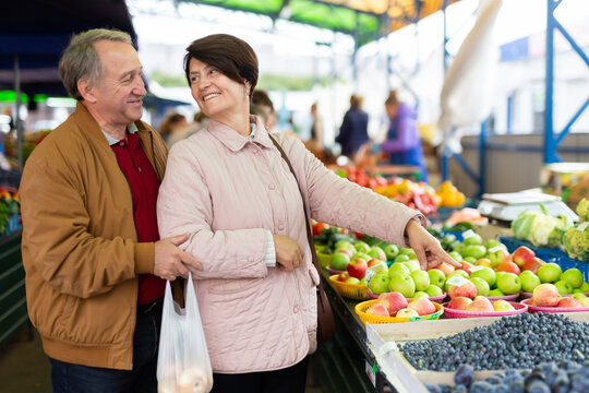 Aged man and woman customers buying berries in open-air market
