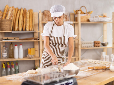 Elderly woman baker cutting dough with scraper