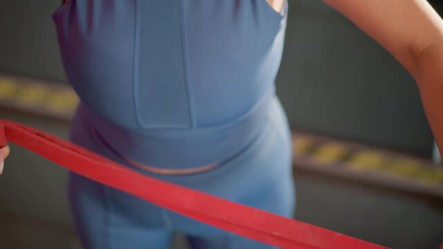 Woman prepares for upper body workout using bright red resistance bands. Woman adjusts elastic straps around her hands focusing on proper positioning before beginning strength training