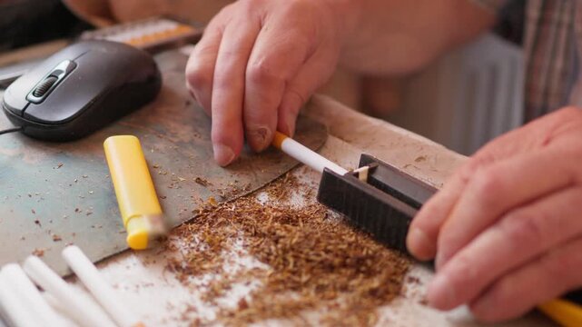 Close up of a person using a manual cigarette rolling machine to fill an empty paper tube with tobacco