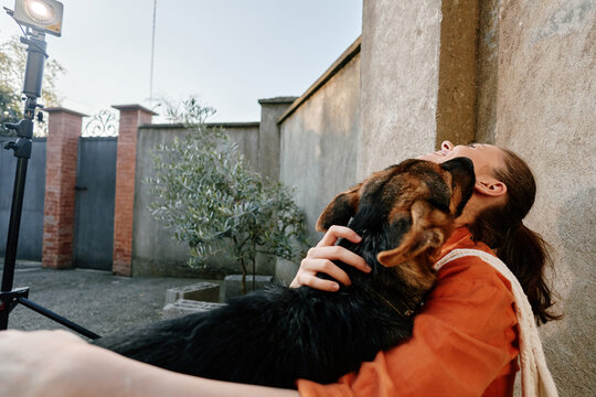 A young woman hugs her loyal dog outdoors near a concrete wall. The friendly pet licks her face happily during a warm afternoon walk. Concept for animal affection and pet lover joy.