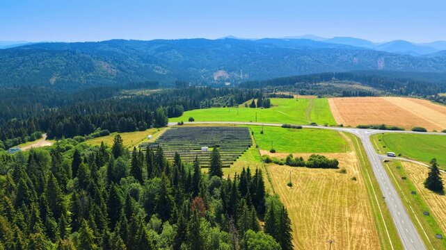 Fields and forest surround a solar array in the Slovak countryside. A road crosses green and gold plots below wooded hills with panel rows visible in an elevated view.